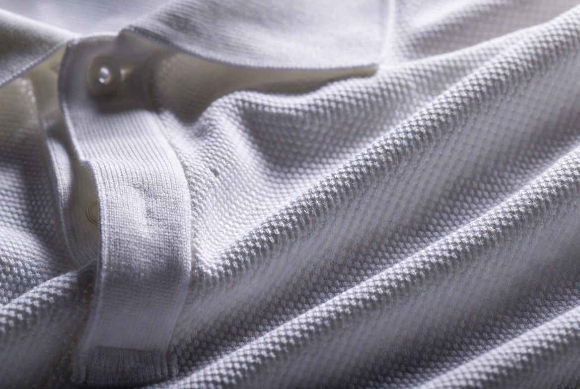 Macro detail of luxurious white petit piqué cotton polo shirt fabric, intricate knit texture and three-button placket — the revolutionary material that changed sports performance forever.